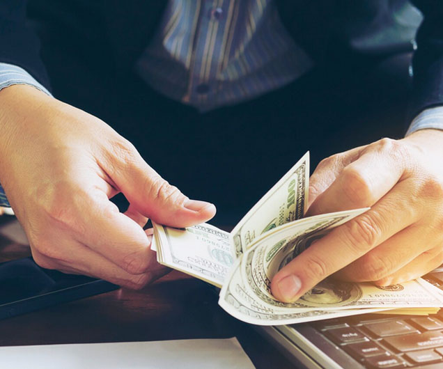 Hands counting cash on a desk with a laptop, illustrating financial transactions related to payday loans in California.