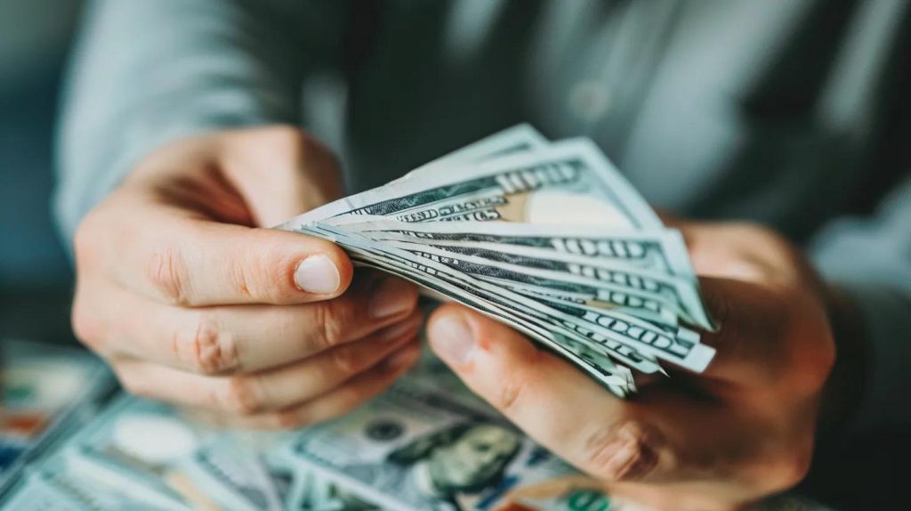 Hands holding cash, featuring multiple hundred-dollar bills, symbolizing fast online loan access in California.